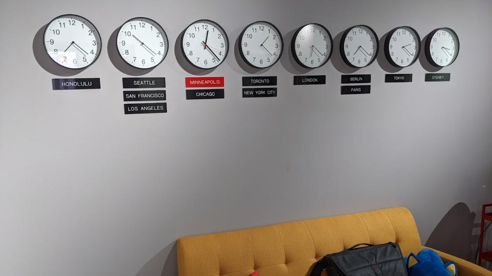 A photo of eight analog clocks on a wall, showing the time for various cities around the world.
